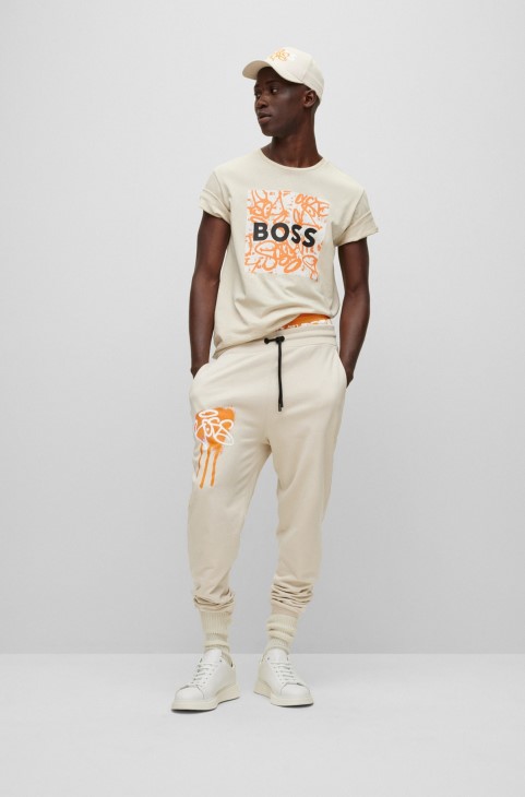 Hugo Boss ανοιχτό μπεζ παντελόνι αθλητικής φόρμας με χαλαρή εφαρμογή με έργα τέχνης γκράφιτι
