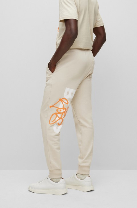 Hugo Boss ανοιχτό μπεζ παντελόνι αθλητικής φόρμας με χαλαρή εφαρμογή με έργα τέχνης γκράφιτι
