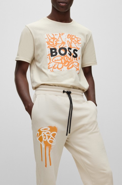 Hugo Boss ανοιχτό μπεζ παντελόνι αθλητικής φόρμας με χαλαρή εφαρμογή με έργα τέχνης γκράφιτι
